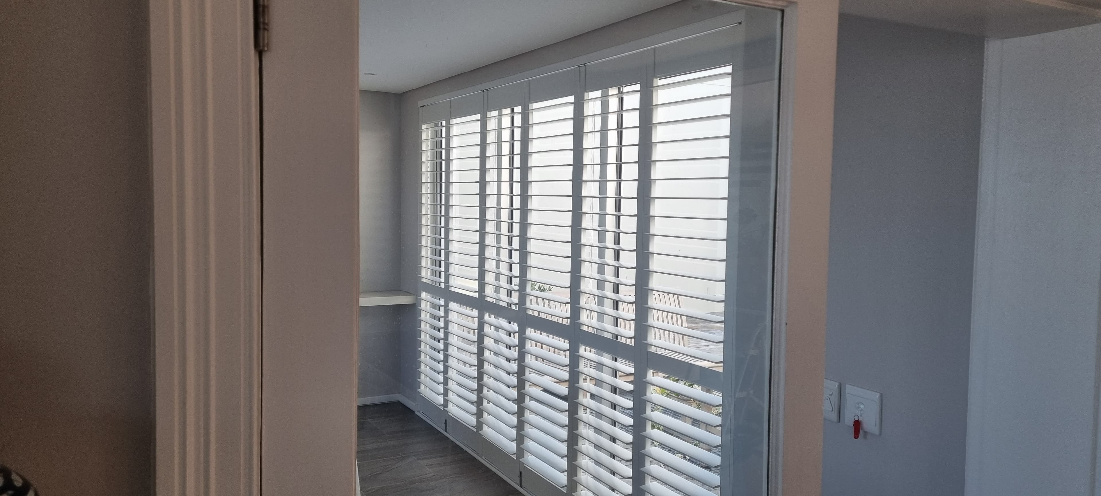 Thermowood PVC folding shutters across a glass sunroom doorway